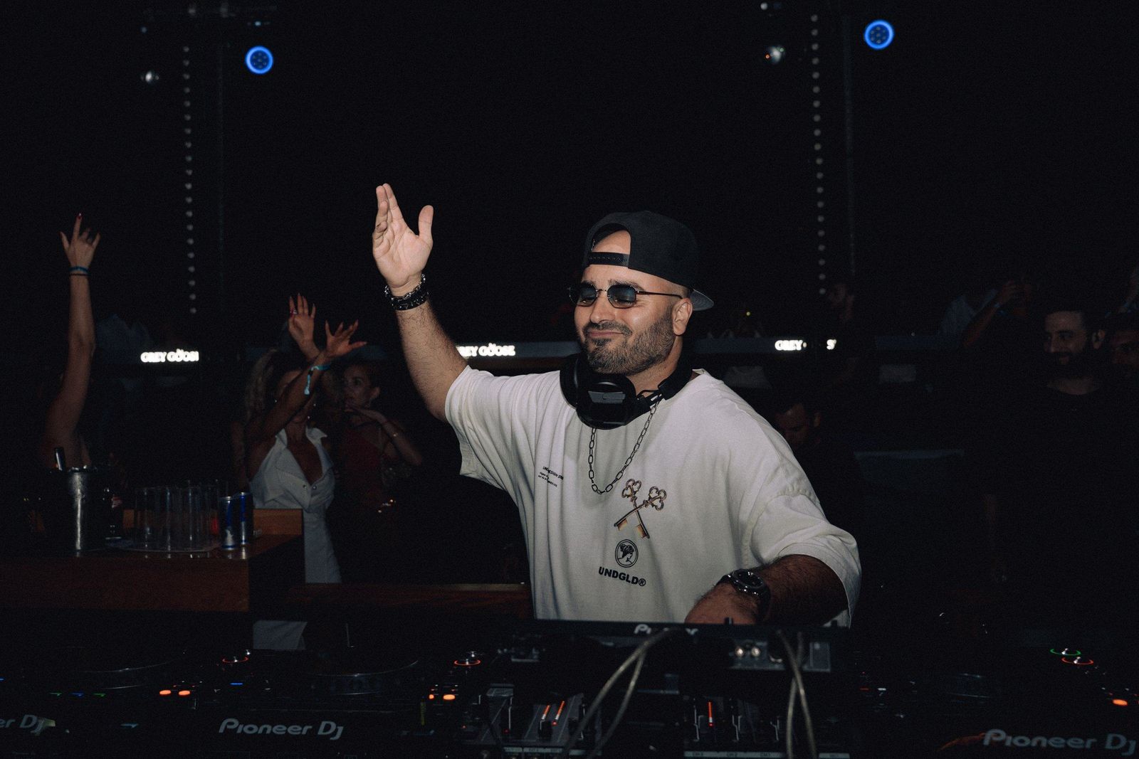 ERAN in a white T-shirt raising his hand at the decks